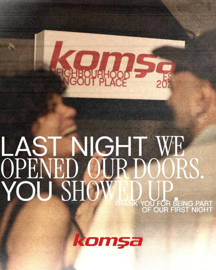 Two people under the lit Komša sign on opening night, grainy archive photo